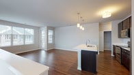 This single-floor residence features a thoughtfully designed open-concept layout that seamlessly connects the kitchen, dining, and living areas. Rich hardwood-style flooring flows throughout the main living spaces, complementing the neutral wall tones and creating a warm, cohesive aesthetic.

The kitchen is a standout feature, centered around a substantial island with a white countertop and integrated sink, illuminated by a trio of pendant lights. Dark espresso cabinetry extends to the ceiling, providing generous storage, while a full suite of stainless steel appliances — including a refrigerator, range, and built-in microwave — adds a polished, modern finish. The adjacent living area benefits from multiple windows that invite natural light and offer views of the surrounding neighborhood.

The bedrooms are carpeted for comfort, with one featuring a spacious walk-in closet and direct access to a private en-suite bathroom equipped with a glass-enclosed shower. A second bathroom includes a full soaking tub and shower combination. Both bathrooms share a consistent design language with dark wood vanities, white countertops, and well-lit vanity mirrors. The overall ambiance is clean, contemporary, and move-in ready.