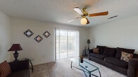 This single-floor residence offers a functional and comfortable layout across several well-defined living spaces. The living room serves as the heart of the home, featuring plush carpeting, a ceiling fan with light fixture, a textured ceiling, and a large sliding glass door fitted with vertical blinds that opens to an outdoor balcony, allowing abundant natural light to fill the room. Adjacent to the living room is a dedicated dining area, accented by colorful wall art and carpeted flooring, providing an intimate space for meals. The galley-style kitchen is equipped with ample white cabinetry with wood-tone trim, white appliances including a refrigerator and dishwasher, and rich hardwood-style flooring that adds warmth to the space. The residence includes two bedrooms, both carpeted and served by ceiling fans or overhead lighting. The primary bedroom features a spacious layout with an en-suite bathroom, while the secondary bedroom benefits from a large window that invites natural light and outdoor views. Two bathrooms serve the home; one includes a tub-shower combination with hardwood-style flooring and a single vanity, while the second offers a wide vanity with a large mirror. Throughout, the home maintains a clean, neutral palette that creates a bright and welcoming atmosphere.