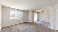 This single-floor residence offers a comfortable and functional layout with a clean, neutral aesthetic throughout. The living areas are finished with plush wall-to-wall carpeting in a warm beige tone, complementing the soft, neutral-painted walls that create a bright and inviting atmosphere. Large windows fitted with vertical blinds allow generous natural light to fill the main living spaces, offering views of the surrounding greenery outside.

The main living area is spacious and open, featuring a ceiling fan with a light fixture, providing both comfort and illumination. A sliding door leads to an additional area, further extending the usable space. The entry area is accented by tile flooring at the threshold, providing a practical transition point into the carpeted interior.

The bedrooms are generously sized, each with carpeted floors, neutral walls, and ample natural light from windows with vertical blinds. One bedroom includes a built-in closet with sliding doors, adding practical storage solutions.

The galley-style kitchen is a standout feature, showcasing warm honey-toned wood cabinetry, dark granite-look countertops, hardwood-style flooring, and black appliances including a gas range, microwave, refrigerator, and dishwasher. Recessed lighting overhead ensures the kitchen is well-lit and functional. The overall space offers a cohesive, move-in ready environment.