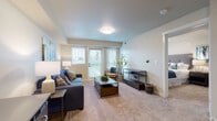 This single-floor unit offers a thoughtfully designed layout that connects the kitchen, living area, bedroom, and bathroom in a cohesive flow. The kitchen is well-equipped with a full suite of stainless steel appliances, including a refrigerator, electric range, built-in microwave, and dishwasher. Rich, dark-stained cabinetry provides generous storage, while light wood-look flooring grounds the space with a clean, contemporary feel. The kitchen opens directly into the living area, creating an inclusive environment suitable for both everyday living and entertaining.

The living room features plush carpeting, neutral-toned walls, and large windows alongside a glass door that opens to a private balcony, allowing natural light to fill the room. The bedroom continues the carpeted flooring and includes a window for additional natural light, as well as a closet for storage.

The bathroom is elongated and functional, featuring dark cabinetry consistent with the kitchen, a wide vanity with a single sink, a large mirror, and a shower-tub combination with a curtain enclosure. Light wood-look flooring carries through this space as well, maintaining visual consistency throughout the unit. Overall, the design balances practicality with a modern, residential aesthetic.