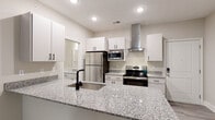 Located at 300 Hickory Trace Ln in Garner, NC, this single-floor residence offers a clean, contemporary design with thoughtfully appointed spaces throughout. The open-concept kitchen serves as the heart of the home, showcasing granite countertops with subtle grey and white veining, crisp white cabinetry with matte black hardware, and a full suite of stainless steel appliances including a refrigerator, electric range, and built-in microwave. A sleek stainless steel wall-mounted range hood adds a modern focal point, while a large kitchen island with an undermount sink provides ample workspace and casual seating potential. Light wood-look luxury vinyl plank flooring extends through the kitchen and living areas, creating a seamless, cohesive flow. The living area is generously proportioned with neutral walls and plush wall-to-wall carpeting, transitioning naturally from the kitchen. Bedrooms are well-sized, featuring carpet flooring, ceiling fans, and windows that invite natural light and views of surrounding greenery. The primary bedroom includes access to a walk-in closet with wire shelving systems and a private bathroom. The full bathroom features a tub-shower combination with tiled surround, light wood-look flooring, and neutral cabinetry with granite countertops, maintaining the home's consistent modern aesthetic.