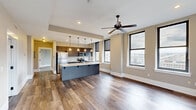 Located at 36 W Federal St in the heart of downtown Youngstown, Ohio, this thoughtfully designed 2-bedroom, 3-bathroom residence offers a well-appointed single-floor layout. The open-concept kitchen and living area serves as the centerpiece of the home, featuring rich hardwood-style flooring, a large central island with a light stone countertop, dark wood cabinetry, stainless steel appliances, and a suite of pendant lights that add warmth and character. A ceiling fan anchors the living space, which is bathed in natural light through multiple large windows fitted with roller shades, framing impressive views of the Youngstown cityscape. The kitchen wall is lined with ample upper and lower cabinetry alongside full stainless steel appliances, combining both form and function. A dedicated hallway connects the private quarters, lined with multiple closets providing generous storage. The two bedrooms are carpeted for comfort, each offering a calm, neutral palette with white panel doors and their own closet space. The generously sized primary bedroom includes a double-door closet. Three bathrooms serve the residence, including one finished with large-format marble-look tile flooring and modern vanity. Throughout, clean white trim and neutral warm-toned walls create a cohesive, contemporary aesthetic.