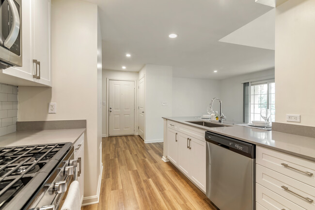 Renovated Package I kitchen with white cabinetry, grey quartz countertops, grey tile backsplash, stainless steel appliances, and hard surface plank flooring - Avalon at The Pinehills