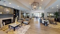 Located at 240 Natoma Station Dr in Folsom, California, this single-story community clubhouse at Waterford Place offers a well-appointed gathering space designed with both comfort and functionality in mind. The welcoming lobby sets an immediate impression with soaring vaulted ceilings, rich wood-look flooring, and a striking geometric pendant chandelier. A cozy seating area anchored by a fireplace and built-in shelving in a sophisticated gray finish invites relaxation, while large glass entry doors flood the space with natural light and provide views of the surrounding outdoors. A corridor leads to multiple functional areas, including private offices and bulletin board stations that serve as a community information hub. The full kitchen is a standout feature, appointed with dark cabinetry, granite countertops, stainless steel appliances, and a spacious island with bar seating illuminated by pendant lighting — ideal for community gatherings and events. The fitness center is generously sized and well-equipped, featuring a broad selection of cardio machines, strength training equipment, free weights, and exercise balls, all set against vibrant teal accent walls with ceiling fans and mirrored walls to enhance the sense of space.