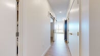 Located at 4757 Hiawatha Ave in Minneapolis, MN, this thoughtfully designed one-bedroom, one-bathroom unit offers a clean, modern aesthetic throughout its compact single-floor layout. The hallway entry sets a bright, contemporary tone with light hardwood-style flooring, crisp white walls, recessed lighting, and a stylish sliding barn door that adds a functional yet design-forward touch. The open-concept living area continues the light flooring and benefits from a large picture window that invites abundant natural light and outdoor views of the surrounding Minneapolis neighborhood. The bedroom features plush carpeting for added comfort and includes a closet with bifold doors, providing practical storage. A secondary carpeted room also offers closet access, adding flexibility to the layout. The bathroom is finished with wood-look vinyl flooring, a white vanity with modern black hardware, brushed nickel fixtures, and a full tub-shower combination with classic white tile surround. A stacked washer and dryer unit is also present within the space, adding everyday convenience. Throughout the unit, the consistent use of neutral tones, clean lines, and modern hardware creates a cohesive and inviting atmosphere well-suited for urban living in Minneapolis.
