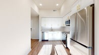 This single-floor unit offers a clean, contemporary design throughout. The open kitchen serves as a central highlight, featuring tall white shaker cabinets with gold-toned hardware extending toward elevated ceilings, complemented by a white subway tile backsplash, light quartz countertops, and a full suite of stainless steel appliances including a refrigerator, electric range, over-the-range microwave, and dishwasher. Recessed lighting and abundant natural light streaming across the wood-look flooring enhance the bright, airy atmosphere of the main living area, which flows openly toward the kitchen.

Two bedrooms each feature the same warm wood-look flooring, neutral walls, and windows that invite natural light and outdoor views. The bathrooms are finished with penny-round mosaic tile flooring and white vanities with gold hardware. One bathroom includes a glass-enclosed walk-in shower with large-format beige wall tiles, while a second offers a more compact layout. A dedicated utility closet houses a stacked washer and dryer alongside the HVAC system, providing practical in-unit convenience. The overall aesthetic is cohesive, modern, and well-appointed.