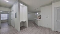 This single-story apartment boasts a contemporary design with an emphasis on open space and functionality. The main living area seamlessly integrates with the kitchen, featuring a white quartz countertop island and stainless steel appliances. Gray wood-look flooring runs throughout, complementing the crisp white walls and trim. The living room is illuminated by natural light from windows and a glass door, while modern ceiling fans and recessed lighting provide additional illumination. A built-in desk nook offers a convenient workspace. The bedroom continues the modern aesthetic with ample space and a large closet. An attached garage provides secure parking and storage. Crown molding and sleek fixtures add refined touches to this stylish urban dwelling.