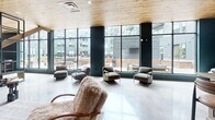 Located at 1143 Main St in Hartford, CT, this generously sized single-floor amenity lounge offers a thoughtfully designed open-plan layout that blends modern industrial aesthetics with warm, inviting materials. The space is defined by striking floor-to-ceiling glass walls that flood the interior with abundant natural light and provide sweeping views of the surrounding courtyard and building exterior. Warm natural wood plank ceilings run throughout, creating a welcoming contrast against the polished concrete floors below. Structural columns finished in a deep teal-green tone punctuate the space and reinforce the contemporary industrial character. A standout feature is the dramatic black steel-framed open staircase and shelving unit, serving as both a functional divider and a sculptural focal point. The lounge is organized into distinct activity zones: a casual seating area furnished with plush sofas and accent chairs, a game zone equipped with a billiards table and ping-pong table, and a cozy lounge nook with a wall-mounted television and exposed blue-gray brick accent wall. A bar-height counter along the brick wall provides a compact workspace or social perch. Steel-framed glass doors connect seamlessly to an outdoor patio area, further extending the sense of openness. The overall ambiance is modern, social, and loft-inspired.