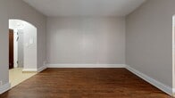 Located at 2425 Delaware Ave in Buffalo, NY, this 2-bedroom, 1-bathroom unit offers a practical and efficient single-floor layout. The space is unified by rich, dark hardwood flooring that flows throughout the living areas and bedrooms, complemented by neutral gray walls and clean white baseboards that create a consistent, understated aesthetic.

The living room is a welcoming entry point, distinguished by elegant arched doorways that lend a classic architectural character to the space. Large windows allow natural light to fill the room, which also features a cast-iron radiator — a nod to the building's traditional construction. An arched passageway connects the living area to the rest of the unit.

Both bedrooms continue the hardwood flooring and neutral palette. Each room includes a window for natural light and ventilation, with cast-iron radiators providing warmth. The primary bedroom includes a closet with rich wood-toned double doors, while the unit also benefits from a total of three closets for ample storage.

The kitchen features warm wood cabinetry, a white range, and a full-size refrigerator, with light-toned flooring that differentiates it from the rest of the unit. The bathroom is clean and functional, offering a shower-tub combination, vanity, and a window for natural light.