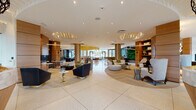 This expansive single-floor amenity space is a showcase of contemporary design, offering a seamless blend of elegance and functionality. The grand entrance greets visitors with terrazzo flooring, warm wood-paneled walls, and floor-to-ceiling glass that floods the space with natural light and provides views of the surrounding landscape.

At the heart of the space is a sweeping open lobby adorned with distinctive sculptural ceiling installations, including a striking cascading gold chain chandelier that anchors the central lounge. This area features an array of curated seating arrangements — from plush sofas and accent chairs to curved lounge islands — designed to encourage both social interaction and relaxed conversation.

A sophisticated bar and dining area includes counter seating with green upholstered stools, a living green wall, and abundant window views. Adjacent to this is a billiards area and a curated entertainment lounge featuring a dramatic dark-ceiling room with hexagonal display shelving, a large media screen, and layered gold pendant lighting.

A dedicated business center and private conference room offer a refined workspace setting with agate art wall accents, a fireplace feature wall, and individual workstations. Additional intimate lounge nooks with bold, patterned furnishings and warm pendant lighting complete the space, creating a dynamic environment that balances productivity with leisure.
