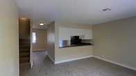 This two-floor residence offers a practical and well-organized layout designed for comfortable everyday living. The main level showcases an open-concept living and kitchen area, where the space flows seamlessly from room to room. The kitchen is appointed with crisp white upper cabinetry, dark countertops, a black refrigerator, and a built-in sink set into a peninsula that doubles as a breakfast bar or prep space. A mirrored backsplash adds a subtle sense of depth and brightness to the cooking area. Light wood-style flooring extends throughout the main living space, complementing the warm, neutral-toned walls that lend a clean and airy feel to the interior. A textured ceiling adds a classic finishing touch. An adjacent hallway connects to additional rooms, with a window at the far end drawing in natural light and enhancing the sense of openness. The overall ambiance is understated and move-in ready, with a straightforward design that provides a versatile canvas for personalization. The second floor expands the living area further, offering additional space well-suited for bedrooms or flexible-use rooms.