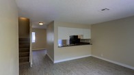This two-floor residence offers a practical and well-organized layout designed for comfortable everyday living. The main level showcases an open-concept living and kitchen area, where the space flows seamlessly from room to room. The kitchen is appointed with crisp white upper cabinetry, dark countertops, a black refrigerator, and a built-in sink set into a peninsula that doubles as a breakfast bar or prep space. A mirrored backsplash adds a subtle sense of depth and brightness to the cooking area. Light wood-style flooring extends throughout the main living space, complementing the warm, neutral-toned walls that lend a clean and airy feel to the interior. A textured ceiling adds a classic finishing touch. An adjacent hallway connects to additional rooms, with a window at the far end drawing in natural light and enhancing the sense of openness. The overall ambiance is understated and move-in ready, with a straightforward design that provides a versatile canvas for personalization. The second floor expands the living area further, offering additional space well-suited for bedrooms or flexible-use rooms.