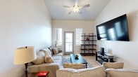 This single-floor space showcases a thoughtfully designed layout that balances modern aesthetics with everyday functionality. The living room serves as the heart of the unit, featuring notably tall, vaulted ceilings that lend an open, airy feel to the space. Light-toned hardwood-style flooring runs throughout, complementing the neutral wall palette. Natural light fills the room through multiple windows and a glass-panel exterior door that opens to a balcony, offering outdoor views. A ceiling fan overhead provides both comfort and style. An open-concept kitchen is outfitted with warm wood-toned cabinetry, white quartz countertops, a classic subway tile backsplash, and a full suite of stainless steel appliances including a refrigerator, range, microwave, and dishwasher. An integrated dining area with a built-in table provides a convenient space for casual meals. The bedroom is a tranquil retreat with high ceilings, large windows for ample natural light, and the same consistent flooring found throughout the unit. The bathroom features a clean, modern design with a wood-accented vanity, white quartz countertop, and a shower with a curtain enclosure. Overall, the space presents a cohesive, contemporary design with a bright and welcoming ambiance.