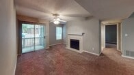 This single-floor residence offers a functional and cohesive layout throughout its interconnected living spaces. The living room serves as the central gathering area, highlighted by a tile-surround fireplace with a classic white mantel, a ceiling fan, and a sliding glass door that opens to an outdoor patio, allowing natural light to fill the room. Adjacent to the living area, the kitchen is designed with efficiency in mind, featuring white cabinetry, dark granite-style countertops, wood-look flooring, and a full suite of black appliances including an electric range, dishwasher, and refrigerator. A pass-through counter connects the kitchen to the main living space, enhancing the open feel. The bedrooms are carpeted and finished in neutral gray tones, with one bedroom offering direct outdoor access via a sliding door and a walk-in closet. A second bedroom provides a windowed view and ample floor space. Both bathrooms are equipped with tub-shower combinations and vanities featuring granite-style countertops, with one bathroom accessible directly from a bedroom. Textured ceilings and consistent neutral wall tones unify the overall aesthetic throughout the space.