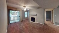 This single-floor residence offers a functional and cohesive layout throughout its interconnected living spaces. The living room serves as the central gathering area, highlighted by a tile-surround fireplace with a classic white mantel, a ceiling fan, and a sliding glass door that opens to an outdoor patio, allowing natural light to fill the room. Adjacent to the living area, the kitchen is designed with efficiency in mind, featuring white cabinetry, dark granite-style countertops, wood-look flooring, and a full suite of black appliances including an electric range, dishwasher, and refrigerator. A pass-through counter connects the kitchen to the main living space, enhancing the open feel. The bedrooms are carpeted and finished in neutral gray tones, with one bedroom offering direct outdoor access via a sliding door and a walk-in closet. A second bedroom provides a windowed view and ample floor space. Both bathrooms are equipped with tub-shower combinations and vanities featuring granite-style countertops, with one bathroom accessible directly from a bedroom. Textured ceilings and consistent neutral wall tones unify the overall aesthetic throughout the space.