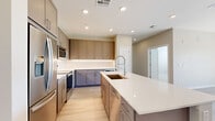 Located in Avondale, Arizona, this well-appointed single-story home offers three bedrooms and three bathrooms within a thoughtfully designed floor plan. The standout kitchen features warm taupe cabinetry, under-cabinet lighting, crisp white quartz countertops, a large center island with a deep basin sink and professional-style faucet, stainless steel appliances, and a built-in beverage cooler — all set atop light wood-look flooring that flows seamlessly throughout the main living areas. The living room is bathed in natural light and opens via sliding glass doors to a private balcony that frames sweeping views of lush greenery and the Arizona mountain landscape beyond. The primary bedroom is generously sized and includes a well-lit en suite bathroom with a long vanity, LED-backlit mirror, and direct access to a walk-in closet with built-in shelving and hanging rods. Two additional bedrooms feature plush carpeting, ceiling fans, and natural light from well-positioned windows. Secondary bathrooms are finished with large-format gray tile surrounds in the tub-shower combinations and clean, modern vanities. Two carpeted walk-in closets provide ample storage throughout. The home's neutral palette and contemporary finishes create a cohesive, move-in-ready aesthetic throughout.