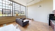 Located at 2320 E Superior Ave in Cleveland, OH, this 4-bedroom, 3-bathroom unit blends industrial character with functional living. The open living and dining area immediately impresses with soaring ceilings, exposed ductwork, and expansive steel-framed factory windows that flood the space with natural light and offer views of the surrounding cityscape. Warm hardwood flooring runs throughout, complementing the raw, loft-inspired aesthetic. Pendant industrial lighting adds to the authentic character of the common areas. The dining area comfortably accommodates a full table set, positioned to take advantage of the generous vertical space and natural light from the large windows. Each of the four bedrooms features hardwood floors, sliding closet doors, and neutral tones, providing a clean and versatile backdrop. The primary bedroom offers a comfortable footprint with additional storage. The three bathrooms are fitted with clean, white stand-up shower enclosures and neutral wall tones. A standout feature is the in-unit stacked washer and dryer, located within a full bathroom that also includes tile flooring and a dark-wood vanity. The overall ambiance is urban and utilitarian, with the converted industrial architecture lending the space a distinctive, loft-like character.