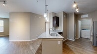 This well-appointed single-floor unit offers a thoughtfully designed open-concept layout that seamlessly connects the kitchen and living areas. The kitchen serves as the centerpiece, featuring a large island with granite countertops and an undermount sink, illuminated by stylish pendant lighting. Dark espresso cabinetry — including glass-front upper cabinets — pairs elegantly with a mosaic tile backsplash and a full suite of stainless steel appliances, including a refrigerator, range, microwave, and dishwasher. Hardwood-style flooring extends throughout the main living areas, adding warmth and continuity to the space.

The bedroom is generously sized, bathed in natural light from large windows, and features a ceiling fan along with plush carpeting underfoot. A spacious walk-in closet with wire shelving provides ample storage. The bathroom is finished with a dark-vanity cabinet, granite countertop, large framed mirror, and a tiled soaking tub and shower combination.

A dedicated laundry area with a full-size washer and dryer adds everyday convenience. Neutral warm-toned walls throughout the unit create a calm, cohesive ambiance, making the space feel open, clean, and move-in ready.