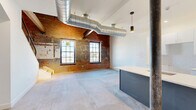 Located at 356 Hertel Ave in Buffalo, NY, this two-story industrial loft blends historic character with modern finishes. The main floor opens into a generous combined living and dining area anchored by polished concrete floors, exposed brick walls, and oversized multi-pane windows that flood the space with natural light. A standout kitchen island with a white quartz countertop and slate-blue cabinetry serves as the centerpiece, complemented by white subway tile backsplash, white upper cabinets, and pendant lighting. A cast-iron structural column and large exposed silver ductwork reinforce the raw, industrial aesthetic. A sleek staircase with a black steel cable railing leads to the upper level, where warm hardwood floors and dramatic exposed brick ceilings with original timber beams define the bedroom loft. A modern shoji-style sliding door provides a stylish entry to the bedroom. The bathroom features marble-look tile flooring, subway-tiled walls, a floating gray vanity with a white countertop, and an LED-backlit mirror. Additional conveniences include in-unit laundry and two closets. The two-floor layout provides a clear distinction between living and sleeping areas within a compact yet efficiently designed footprint.