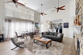 Located at 15235 O'Neal Rd in Gulfport, Mississippi, this single-floor space makes a striking impression with its dramatic, soaring ceilings that visually expand the open-concept main area. Multiple ceiling fans are suspended at varying heights, complementing the abundant natural light that streams in through large windows dressed with sheer curtains and horizontal blinds — including a distinctive arched transom window positioned high on the wall near the fireplace.

The centerpiece of the main living area is a floor-to-ceiling stone fireplace, a bold architectural feature that anchors the room and adds warmth and character. The open layout comfortably accommodates distinct living, dining, and workspace zones, all unified by durable wood-look plank flooring throughout. The neutral white walls provide a clean, versatile backdrop.

The kitchen is efficiently designed in a U-shaped configuration, featuring granite countertops, white cabinetry, open display shelving, and black appliances including a gas range and full-size refrigerator. A raised breakfast bar with bar stool seating connects the kitchen to the main living area, making it both functional and social. Track lighting overhead ensures the kitchen is well-lit. An additional room off the main area offers flexible use as an office, bedroom, or private retreat, complete with its own window and door access.