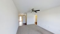 This single-floor residence offers a clean, neutral aesthetic with an open and airy layout. The main living area is finished with plush wall-to-wall carpeting that adds warmth underfoot, while adjacent spaces transition to smooth hard flooring, providing both comfort and practicality. Crisp white walls throughout create a bright, welcoming atmosphere that feels open and easy to personalize.

A ceiling fan with a built-in light fixture is centrally positioned in the main living area, ensuring year-round comfort and efficient air circulation. The layout features a partial dividing wall that subtly separates living zones while maintaining an open feel between spaces.

Natural light filters in through a front entry door with a window, illuminating the entryway and hallway areas. The entry corridor leads seamlessly into the main living space, with additional rooms accessible via interior doorways. Vaulted or elevated ceilings add a sense of spaciousness and volume to the interior.

Overall, the space presents a functional and well-maintained environment with a straightforward floor plan, neutral finishes, and practical features that make it move-in ready and adaptable to a variety of living styles.