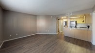 This single-floor residence offers a practical and well-organized layout designed for comfortable everyday living. The open living area features rich, dark hardwood-style flooring, neutral taupe walls, and a textured ceiling, creating a clean and inviting atmosphere. A window with blinds allows natural light to fill the space, enhancing its airy feel.

The kitchen is efficiently designed with warm wood cabinetry, speckled laminate countertops, and a full suite of black appliances including a refrigerator, electric range with overhead ventilation, and a stainless steel sink. Overhead fluorescent lighting ensures the workspace is well-lit throughout the day.

The bedrooms are finished with soft wall-to-wall carpeting in a neutral tone, complemented by the same taupe wall color found throughout the home. Each room provides a calm, restful environment, with windows dressed in blinds offering natural light and privacy.

The bathroom is thoughtfully appointed, featuring a wood-toned vanity with a speckled countertop and undermount sink, a large mirror with overhead vanity lighting, and a white tub-shower combination with clean surround panels. The hardwood-style flooring in the bathroom ties cohesively to the rest of the home. A second bathroom includes a tub-shower combo and maintains the same clean, functional aesthetic. Overall, the space presents a consistent, neutral design throughout.