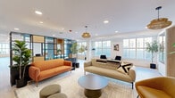 Located at 601 N Broad St in Philadelphia's vibrant Northern Liberties neighborhood, this single-floor communal space is a masterclass in contemporary interior design. The open, flowing layout is anchored by light hardwood flooring throughout and bathed in natural light from an abundance of large windows offering street-level views of the surrounding cityscape.

The space is organized into several distinct yet interconnected zones. A sophisticated lounge area features a bold orange velvet sofa paired with a neutral counterpart, complemented by a woven pendant light and vibrant abstract artwork. Adjacent to this, a sleek steel-framed glass partition with built-in shelving elegantly separates zones while maintaining visual openness. Potted fiddle-leaf fig and olive trees are positioned throughout, adding a lush, organic element.

A dedicated activity and dining area includes a communal table with ample seating beneath a sculptural multi-globe chandelier, flanked by arched green cabinetry and whimsical accent seating. A teal-accented nook offers a vibrant retreat with built-in shelving, a plush sofa, and illuminated display features. Warm wood arched built-ins provide cozy reading alcoves. A media lounge with a wall-mounted display, open shelving, and soft bucket chairs rounds out the space, offering a quieter setting for relaxation or casual gatherings.