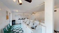 This shared laundry facility is designed to accommodate the needs of multiple users efficiently. The space features a row of top-loading washing machines positioned along a central island, providing convenient access from both sides. Along the back wall, a bank of stacked dryers offers ample drying capacity. The machines are finished in white, contributing to a clean, uniform appearance throughout the room.

The flooring consists of a classic green and white checkered tile pattern, adding a distinctive visual element to the utilitarian space. Overhead, the white ceiling is fitted with a ceiling fan that aids in air circulation, helping to manage humidity and maintain comfort during use. Additional lighting fixtures are mounted on the ceiling to ensure the room is well-lit.

The walls are painted white, keeping the space bright and easy to maintain. Informational signage is posted near the machines, offering users guidance on proper operation. A waste bin is available near the entrance for added convenience. Overall, the facility is straightforward and functional, providing residents with everything needed for a complete laundry experience.