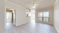 This well-appointed single-floor residence offers a clean, neutral aesthetic throughout, with an open and airy feel enhanced by large windows that invite abundant natural light. The living area features light wood-style flooring, crown molding, and a ceiling fan, creating a comfortable and functional space. A pass-through opening connects the living area to the kitchen, which is equipped with warm honey-toned wood cabinetry, a black appliance suite including a refrigerator, electric range, and over-the-range microwave, as well as light stone-finish countertops. The kitchen flows seamlessly from the main living space, supported by light wood flooring for continuity. The bedrooms are carpeted for comfort, each featuring ceiling fans and windows that allow for natural light and outdoor views. One bedroom includes a generously sized walk-in closet outfitted with wire shelving and hanging rods, offering ample storage. The bathroom features warm wood cabinetry, a wide vanity with a single-basin sink, light stone countertops, and a tub-shower combination. Throughout the space, neutral tones, clean lines, and practical finishes come together to create a cohesive and inviting living environment.