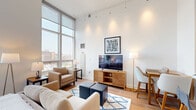 Located on the 10th floor at 200 West Washington Square in Philadelphia's historic Washington Square West neighborhood, this thoughtfully designed unit offers an efficient yet comfortable single-floor layout. The open-concept living and kitchen area is immediately distinguished by impressively tall ceilings and a dramatic floor-to-ceiling window wall that floods the space with natural light and frames sweeping views of the Philadelphia skyline. Light hardwood flooring runs throughout the living area, contributing to an airy, modern ambiance. The kitchen is well-appointed with warm maple cabinetry, granite-look countertops, and a full suite of stainless steel appliances, including an electric range, over-the-range microwave, and refrigerator. A peninsula countertop provides a natural transition into the dining and living area, creating a cohesive, open flow. The bathroom features a classic combination tub and shower with a charming checkered tile surround in neutral tones. A dedicated laundry area accommodates a stacked washer and dryer unit, adding everyday convenience. Two hallways connect the rooms and provide additional circulation space, making the layout feel organized and functional despite its compact footprint.