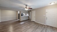 This single-floor residence at 701 Kessler Court in Garden City, Georgia offers a well-organized layout designed for comfortable everyday living. The open living area features wood-look vinyl plank flooring, a textured ceiling, and a ceiling fan with light fixture. A sliding glass door floods the space with natural light while providing direct access to an outdoor balcony with views of surrounding greenery. The kitchen connects seamlessly to the living space and is equipped with granite-look countertops, white cabinetry with brushed nickel hardware, a dark subway tile backsplash, and black appliances including an electric range with an over-the-range microwave. A dedicated laundry closet houses a full-size washer and dryer with overhead shelving for additional storage. The bedrooms are carpeted for comfort, each featuring ceiling fans and windows that bring in natural light. The bathroom is finished with matching granite-look countertops, white cabinetry, brushed nickel fixtures, and wood-look vinyl plank flooring, complemented by a full shower-tub combination. Neutral tones throughout create a cohesive and inviting atmosphere.