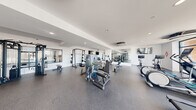 Located at Anthony Ave in Mundelein, IL, this fitness center offers a generously sized, single-floor exercise room designed to support a full range of workout routines. The space features a clean, modern aesthetic with crisp white walls, recessed lighting, and durable rubber flooring throughout, creating a bright and functional environment.

The cardio zone is anchored by large floor-to-ceiling windows that flood the area with natural light and provide outdoor views, housing treadmills, elliptical trainers, and stationary bikes. Ceiling-mounted HVAC units ensure comfortable climate control across the entire floor.

The strength training section is well-appointed with a cable machine, multi-use weight stations, adjustable benches, a free weight rack, and plate-loaded equipment. Full-length wall mirrors extend across key sections of the room, enhancing the sense of space while allowing users to monitor their form.

A dedicated functional training area includes a rack of stability balls in assorted sizes, medicine balls, and kettlebells, providing ample options for flexibility and cross-training workouts. A reception desk near the entrance adds a professional touch, while a locker area supports convenience for users. Mounted flat-screen televisions are positioned throughout the space for added amenity during workouts.