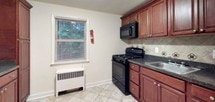 This single-floor residence offers a clean, well-maintained interior characterized by warm hardwood flooring that flows throughout the living and bedroom areas, finished to a high sheen that reflects natural light pouring in from multiple windows. The living spaces are bright and open, painted in neutral tones with white trim and baseboards, and illuminated by recessed ceiling lighting. Each room benefits from windows framing views of surrounding greenery, contributing to a calm and airy atmosphere. Baseboard and wall-unit heating systems are present throughout, ensuring year-round comfort. The kitchen is outfitted with rich, dark wood cabinetry, granite-toned countertops, a tiled backsplash in a classic diamond pattern, and black appliances including a gas range and over-the-range microwave. Light ceramic tile flooring grounds the kitchen's functional layout. The bathroom is neatly finished with diagonal-set tile on both the walls and floor, a full soaking tub enclosed by sliding glass doors, and a white vanity with an integrated sink and mirrored medicine cabinet above. Overall, the space presents a practical and comfortable interior with consistent finishes throughout.