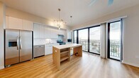 Located at 4331 34th St S in Saint Petersburg, FL, this thoughtfully designed one-bedroom, one-bathroom unit offers a clean, modern aesthetic across its single floor. The open-concept kitchen and living area serves as the heart of the home, showcasing sleek white cabinetry that extends to the ceiling, stainless steel appliances, and a wood-accented island with built-in shelving and a white quartz countertop. Light wood-tone flooring runs throughout the main living space, complementing the bright, airy atmosphere. Floor-to-ceiling sliding glass doors flood the area with natural light and lead directly to a private balcony, offering expansive elevated views of the Saint Petersburg skyline and surrounding neighborhood. The bedroom features neutral wall tones and plush carpet, providing a quiet and comfortable retreat with a dedicated closet. The bathroom is finished in a crisp, minimalist style with large-format floor tiles, a frameless glass walk-in shower, white wall surrounds, and a floating vanity with a white countertop. Additional conveniences include an in-unit laundry area, an entrance foyer, and a dedicated closet. Track and pendant lighting throughout the main living area adds both function and a refined design touch to this well-appointed urban residence.
