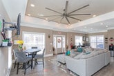 Located at 395 Raven Ridge Dr in Kernersville, NC, this single-floor space is thoughtfully designed with a combination of elegant architectural details and functional living areas. The layout flows seamlessly from one area to the next, all unified by warm, neutral taupe wall tones and durable hardwood-style flooring throughout.

The centerpiece of the space is a generously sized living area distinguished by a striking tray ceiling with crown molding and recessed lighting, lending a sense of architectural depth and refinement. A ceiling fan adds practical comfort. The room accommodates a large sectional sofa arrangement centered on a decorative area rug, creating an inviting gathering space. Natural light filters in through multiple windows fitted with plantation shutters.

A set of elegant French doors with glass pane inserts serves as a notable architectural feature, connecting areas of the space while maintaining a sense of openness. Crown molding continues throughout, reinforcing the polished aesthetic.

A dedicated dining nook is surrounded by windows on two sides, filling the area with abundant natural light. The space comfortably seats a round dining table with upholstered chairs accented with brass nail-head trim, giving the area a refined, intimate feel. Wall sconces and thoughtful décor details further enhance the overall ambiance of this well-designed space.