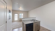 This single-floor unit offers a thoughtfully designed open-concept layout that seamlessly connects the kitchen and living area. The kitchen is outfitted with granite-look countertops, warm wood-toned cabinetry, and a full suite of Whirlpool appliances including an electric range, over-the-range microwave, dishwasher, and refrigerator. A peninsula with an overhang provides additional seating and acts as a natural divider between the kitchen and the carpeted living space. Wood-look vinyl flooring runs through the kitchen and entryway, adding warmth and durability to high-traffic areas. The living area benefits from natural light streaming through a front-facing window and door, creating a bright and welcoming atmosphere. A wall-mounted HVAC unit ensures year-round climate control. A built-in murphy bed with integrated shelving maximizes flexibility in the sleeping area, which features plush carpet and its own exterior-facing window and door. The bathroom is clean and functional, finished with tile flooring and accented by an arched ceiling detail that adds a subtle architectural touch. Neutral tones and a textured ceiling throughout the unit contribute to a fresh, move-in-ready aesthetic.