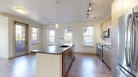 Located at 1910 S Josephine St in Denver, CO, this well-appointed two-bedroom, two-bathroom residence offers a thoughtfully designed single-level layout. The open-concept kitchen and living area serves as the heart of the home, showcasing a large central island with a dark countertop, undermount sink, and pendant lighting. Warm wood-tone cabinetry, a subway tile backsplash, stainless steel appliances, and track lighting complete the kitchen's modern aesthetic. Hardwood-style flooring flows throughout the main living areas, bathed in natural light from multiple double-hung windows with views of the surrounding neighborhood. A glass door leads to a private balcony, extending the living space outdoors. The hallway connects the two carpeted bedrooms, each offering a calm, neutral palette; the primary bedroom includes a ceiling fan and dual windows, while the en-suite bathroom features a double-sink vanity with dark countertops, wood-grain cabinetry, large-format tile flooring, and a glass-enclosed shower. The second bathroom mirrors the same refined finishes. A dedicated laundry area with a full-size washer and dryer adds everyday convenience. Five closets throughout provide generous storage, rounding out this functional and stylish Denver residence.