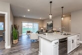 This well-designed single-floor residence offers a thoughtfully planned open-concept layout that seamlessly connects the kitchen, dining, and living areas. The kitchen is a standout feature, showcasing white shaker cabinetry, granite countertops, stainless steel appliances, and a large center island with bar seating for three, illuminated by sleek pendant lighting. Wood-look plank flooring runs throughout the main living areas, adding warmth and continuity to the space.

The living room is bright and inviting, with large sliding glass doors fitted with vertical blinds that allow abundant natural light and provide access to outdoor views. The open layout creates a generous sense of space ideal for both relaxing and entertaining.

The bedrooms are carpeted for comfort, each featuring windows that bring in natural light. The primary bedroom offers ample room and connects to a private bathroom with granite countertops, wood-look flooring, and a spacious walk-in closet. An additional bedroom provides flexibility for guests or a home office.

A dedicated laundry area is also present within the unit. The overall aesthetic blends neutral tones, modern fixtures, and clean architectural lines, creating a cohesive and contemporary living environment throughout.