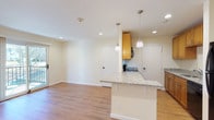 This single-floor, one-bedroom, one-bathroom residence offers a thoughtfully designed layout with consistent finishes throughout. The open-concept living and dining area is finished with warm hardwood-style flooring and neutral walls, creating a bright, welcoming atmosphere. A sliding glass door leads to a private balcony, allowing natural light to fill the space and providing outdoor views.

The kitchen is positioned adjacent to the living area and features a peninsula with granite countertops and pendant lighting overhead, offering both prep space and a casual seating option. Warm-toned wood cabinetry lines both sides of the galley-style kitchen, complemented by black appliances including an electric range with overhead microwave and a full-size refrigerator. A dedicated in-unit laundry area is conveniently tucked nearby, housing a stacked washer unit.

The bedroom is a comfortable, well-proportioned room with hardwood-style flooring, a window allowing natural light, and neutral walls. The full bathroom includes a dark wood vanity with a granite countertop, a framed mirror, tile flooring, and a tub-shower combination with floor-to-ceiling stone-look tile surround.