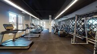 Located at 901 H St NE in Washington, DC, this fitness center is a thoughtfully designed, single-floor facility that delivers a comprehensive workout environment. The space is characterized by a sleek, industrial aesthetic, featuring a dramatic dark ceiling with linear LED lighting that runs the length of the room, creating a focused and energetic atmosphere. Rubber flooring throughout provides both durability and comfort underfoot.

The cardio zone houses a generous row of Life Fitness treadmills and elliptical machines aligned along the perimeter, with multiple windows allowing ample natural light and views of the surrounding neighborhood. A decorative hexagonal tile accent wall adds a refined architectural touch to this area.

The strength training section is equally well-appointed, featuring a multi-station Life Fitness cable machine, weight benches, a full rack of dumbbells, and various free weight and functional training equipment. A large glass door opens directly to an outdoor area, further enhancing the sense of openness and connectivity to the exterior.

Mirror panels and a decorative diamond-pattern wall partition define zones within the space while visually expanding the room. The overall design balances form and function, making this fitness center a standout amenity that supports a wide range of workout routines in an inviting, modern setting.