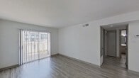 This single-floor unit presents a clean, modern aesthetic defined by bright white walls, textured ceilings, and consistent wood-look laminate flooring that runs throughout the entire space. The living area is generously proportioned, featuring a large sliding glass door dressed with vertical blinds that invites abundant natural light and provides access to the outdoors. A separate entry area with a small raised step platform and a window adds a welcoming transition into the main living space.

The galley-style kitchen is efficiently designed with gray cabinetry, white subway tile backsplash, light countertops, a double stainless steel sink, and black appliances including a range and refrigerator. The layout maximizes functionality within a compact footprint.

The bedroom is bright and well-lit, benefiting from two windows positioned on adjacent walls that allow natural light to fill the room from multiple directions, creating an airy and comfortable atmosphere.

The bathroom is neatly appointed with a tub-shower combo featuring white tile surround, a curved shower rod, a vanity with sink, and wood-look flooring that complements the rest of the unit. A grab bar is also installed for added accessibility.

Overall, this unit offers a cohesive, freshly updated interior with a neutral palette that provides a versatile and move-in-ready living environment.