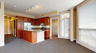 Located at Crocker Park in Westlake, Ohio, this single-floor residence offers a thoughtfully designed layout with a cohesive blend of warm finishes and functional living spaces. The open-concept kitchen is a standout feature, showcasing rich cherry wood cabinetry extending floor to ceiling, dark granite countertops, hardwood flooring, and a full suite of stainless steel appliances including a refrigerator with ice maker, electric range, and built-in microwave. A central island with seating provides both prep space and a casual dining option. The kitchen flows seamlessly into the living area, which is finished with plush carpeting and neutral warm-toned walls, creating a welcoming atmosphere. Track lighting throughout enhances visibility and adds a modern touch. The primary bedroom is generously sized and features a walk-in closet with built-in wire shelving for ample storage. Two bathrooms serve the residence: a primary bath with a glass-enclosed walk-in shower adorned with multicolored mosaic tile accents and a granite vanity, and a second full bath with a tub-shower combination and matching granite countertop. A dedicated hallway laundry nook with stacked washer and dryer adds everyday convenience. Natural light filters in through windows, contributing to the bright and inviting character of the space.