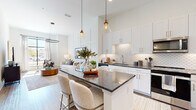 Located at 4271 Woodward Mill Rd in Buford, Georgia, this single-story residence showcases a thoughtfully designed open-concept layout that seamlessly connects the kitchen, dining, and living areas. The kitchen is a standout feature, boasting crisp white shaker cabinetry with gold hardware, dark granite countertops, a decorative scalloped tile backsplash, and a full suite of stainless steel appliances. A central island with built-in shelving provides additional prep space and casual seating, illuminated by stylish pendant lights that hang from soaring ceilings. The living room exudes sophistication with its board-and-batten accent wall, hardwood-style flooring, and an elegant circular chandelier. Natural light pours through large windows, enhancing the bright, airy atmosphere throughout. The bedroom is generously proportioned, featuring plush carpeting, tall ceilings, and an expansive floor-to-ceiling window that frames outdoor views. The bathroom offers a clean, contemporary aesthetic with wood-look flooring, a granite vanity, and a tub surround clad in marble-style tile. Throughout the space, a consistent palette of whites, warm neutrals, and gold accents creates a cohesive, modern ambiance.