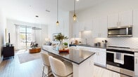 Located at 4271 Woodward Mill Rd in Buford, Georgia, this single-story residence showcases a thoughtfully designed open-concept layout that seamlessly connects the kitchen, dining, and living areas. The kitchen is a standout feature, boasting crisp white shaker cabinetry with gold hardware, dark granite countertops, a decorative scalloped tile backsplash, and a full suite of stainless steel appliances. A central island with built-in shelving provides additional prep space and casual seating, illuminated by stylish pendant lights that hang from soaring ceilings. The living room exudes sophistication with its board-and-batten accent wall, hardwood-style flooring, and an elegant circular chandelier. Natural light pours through large windows, enhancing the bright, airy atmosphere throughout. The bedroom is generously proportioned, featuring plush carpeting, tall ceilings, and an expansive floor-to-ceiling window that frames outdoor views. The bathroom offers a clean, contemporary aesthetic with wood-look flooring, a granite vanity, and a tub surround clad in marble-style tile. Throughout the space, a consistent palette of whites, warm neutrals, and gold accents creates a cohesive, modern ambiance.