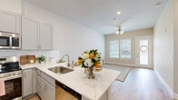 Located in Conroe, TX, this well-appointed one-bedroom, one-bathroom residence offers a smart, efficient layout across a single floor. The open-concept kitchen is a standout feature, showcasing quartz countertops with subtle veining, gray shaker-style cabinetry, a white subway tile backsplash, stainless steel appliances including a French door refrigerator and dishwasher, and a peninsula with a stainless undermount sink — ideal for both cooking and casual dining. The kitchen flows naturally into the living area, which is brightened by a ceiling fan and windows overlooking the community grounds. Light wood-look flooring runs throughout the main living spaces, lending warmth and continuity. The bedroom offers a comfortable footprint, natural light through a window with blinds, and direct access to a generously sized walk-in closet equipped with dual hanging rods and built-in shelving. The full bathroom features gray vanity cabinetry with a white countertop, a tub-shower combination, and wood-look flooring. A dedicated laundry area adds everyday convenience. The covered patio, framed by black metal railings and cheerful exterior siding, provides a pleasant outdoor retreat with views of the landscaped community, complete with palm trees and well-maintained green spaces.