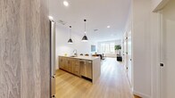 This well-appointed one-bedroom, one-bathroom residence in Norwalk, Connecticut offers a thoughtfully designed open-concept layout that seamlessly connects the kitchen, dining, and living areas. The kitchen is a standout feature, equipped with stainless steel appliances, warm wood cabinetry, and a large quartz-topped island with bar seating, illuminated by striking black pendant lights. Light hardwood flooring flows throughout the main living areas, complementing the crisp white walls and recessed lighting that give the space a bright, airy feel. The living room is generously proportioned, bathed in natural light streaming through a large multi-pane window that frames views of the surrounding neighborhood. The bedroom is a serene retreat finished with plush carpet, oversized windows, and ample space for furnishings. A dedicated walk-in closet with wire shelving provides practical storage. The bathroom features a sleek, modern aesthetic with a sliding glass-enclosed walk-in shower, large-format white tiles, a dark vanity with a quartz countertop, and a frameless mirror. The overall design balances contemporary minimalism with warm, inviting touches throughout.