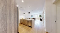 This well-appointed one-bedroom, one-bathroom residence in Norwalk, Connecticut offers a thoughtfully designed open-concept layout that seamlessly connects the kitchen, dining, and living areas. The kitchen is a standout feature, equipped with stainless steel appliances, warm wood cabinetry, and a large quartz-topped island with bar seating, illuminated by striking black pendant lights. Light hardwood flooring flows throughout the main living areas, complementing the crisp white walls and recessed lighting that give the space a bright, airy feel. The living room is generously proportioned, bathed in natural light streaming through a large multi-pane window that frames views of the surrounding neighborhood. The bedroom is a serene retreat finished with plush carpet, oversized windows, and ample space for furnishings. A dedicated walk-in closet with wire shelving provides practical storage. The bathroom features a sleek, modern aesthetic with a sliding glass-enclosed walk-in shower, large-format white tiles, a dark vanity with a quartz countertop, and a frameless mirror. The overall design balances contemporary minimalism with warm, inviting touches throughout.