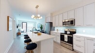 Located at 20 Burling Ln in New Rochelle, NY, this thoughtfully designed single-floor residence seamlessly blends contemporary style with everyday functionality. The open-concept kitchen is a standout centerpiece, featuring crisp white shaker cabinetry, a soft aqua glass tile backsplash, quartz countertops, and stainless steel appliances. A large waterfall-edge island with an integrated sink and bar seating is crowned by a striking gold multi-globe chandelier, making it ideal for both cooking and entertaining. The kitchen flows effortlessly into the living area, which is bathed in natural light from large windows and a glass door leading to an outdoor balcony. The living space offers a comfortable, modern ambiance with light hardwood-style flooring throughout. The bedroom is a serene retreat, highlighted by a bold deep-blue accent wall, large windows that bring in natural light, and clean, neutral walls that complement the warm wood tones of the furnishings. The bathroom features elegant marble-look tile flooring, a glass-enclosed walk-in shower, a wide vanity with white cabinetry, and a bold navy accent wall that adds a sophisticated, cohesive design touch throughout the residence.