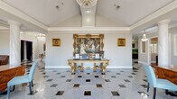 Located at 10801 Paul Eells Dr in North Little Rock, Arkansas, this single-floor space makes a striking first impression with its grand reception area showcasing polished hexagonal black-and-white tile flooring, soaring vaulted ceilings, and an ornate crystal chandelier. A gilded console table beneath an elaborately framed oil painting sets a refined, classical tone throughout.

The reception and corridor areas continue the elegance with additional crystal chandeliers, gold-accented console tables, and decorative mirrors, all framed by pristine white crown molding. Natural light filters through large windows, enhancing the bright, welcoming atmosphere.

The space includes a well-appointed kitchen and bar area featuring rich warm-toned wood cabinetry, dark granite countertops, stainless steel appliances, and a spacious island with ornate wrought-iron bar seating. Granite tile flooring and ample natural light from oversized windows make this a highly functional catering or entertainment hub.

A recreation and lounge area offers rich hardwood floors, a classic fireplace with an ornate carved surround set against a bold teal accent wall, a full-size billiard table, and comfortable leather seating. Throughout, classical artwork, gilded furnishings, and detailed millwork reinforce the space's distinguished, upscale character—making it well-suited for events, gatherings, or professional use.