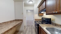 Located at 4339 Riverside Dr. in Dayton, Ohio, this single-floor unit offers a straightforward and practical layout designed for comfortable everyday living. The kitchen is well-equipped with rich, dark wood cabinetry providing ample storage, stone-patterned laminate countertops, a double stainless steel sink, a black electric range with overhead ventilation, and wood-look vinyl flooring that extends through the space. A pass-through corridor connects the kitchen to the rest of the unit. The living area is bright and open, featuring neutral carpet, clean white walls, and a large sliding window with an attached entry door that allows natural light to fill the room. The bedrooms are carpeted and offer generous wall space, with one room featuring a double sliding-door closet for added storage. The bathroom is neatly appointed with wood-look tile flooring, a white vanity with under-cabinet storage, and a full tub-shower combination with white tile surround. A dedicated utility area houses the mechanical systems, including visible plumbing infrastructure, providing convenient access for maintenance. Overall, the unit presents a clean, functional design with consistent finishes throughout.